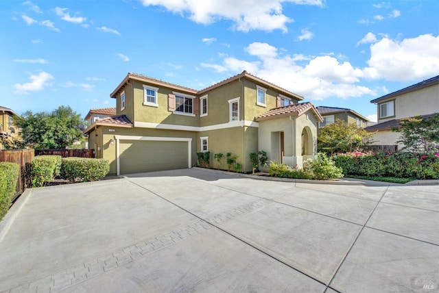 mediterranean / spanish house with a tile roof, stucco siding, an attached garage, fence, and driveway