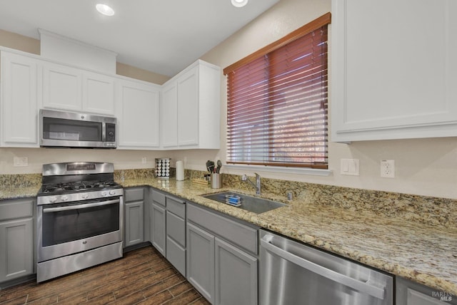 kitchen with dark wood finished floors, light stone countertops, stainless steel appliances, gray cabinetry, and a sink