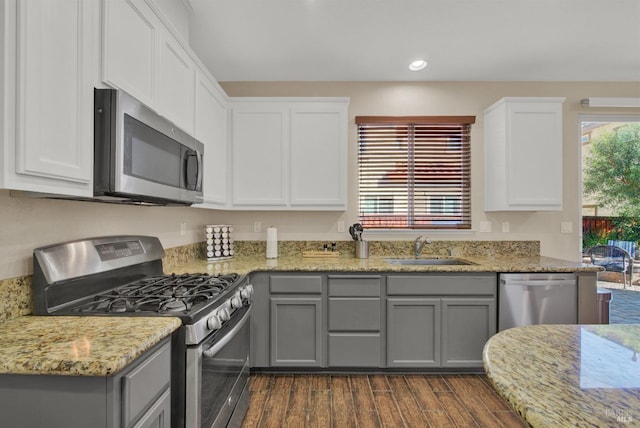 kitchen featuring dark wood finished floors, light stone counters, gray cabinets, stainless steel appliances, and a sink