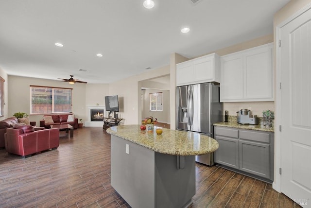 kitchen with wood tiled floor, a kitchen island, a lit fireplace, and stainless steel fridge with ice dispenser