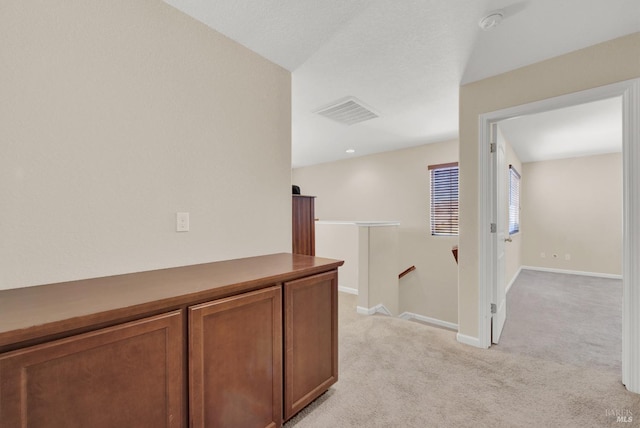 hall featuring baseboards, light colored carpet, visible vents, and an upstairs landing