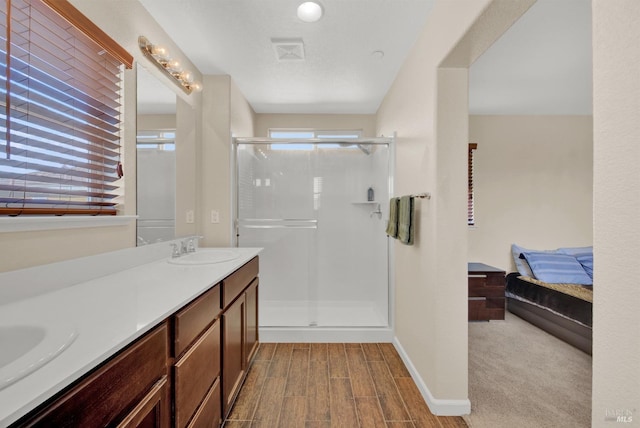 ensuite bathroom featuring connected bathroom, a sink, wood finished floors, visible vents, and a stall shower