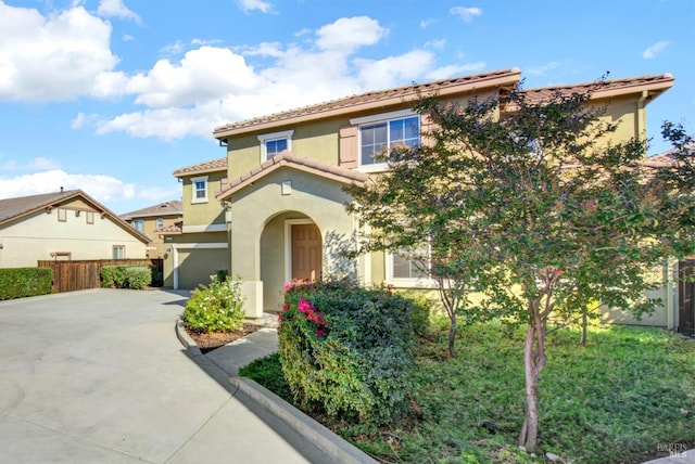 mediterranean / spanish home featuring concrete driveway, a tile roof, an attached garage, fence, and stucco siding