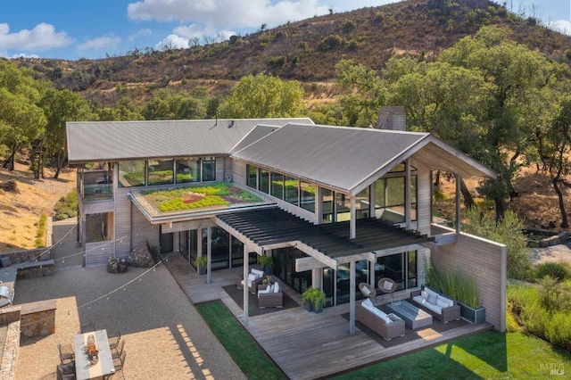 rear view of house featuring a deck with mountain view, a chimney, stairway, and an outdoor living space
