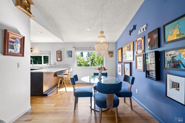 dining space with baseboards, a textured wall, light wood-style flooring, and a textured ceiling