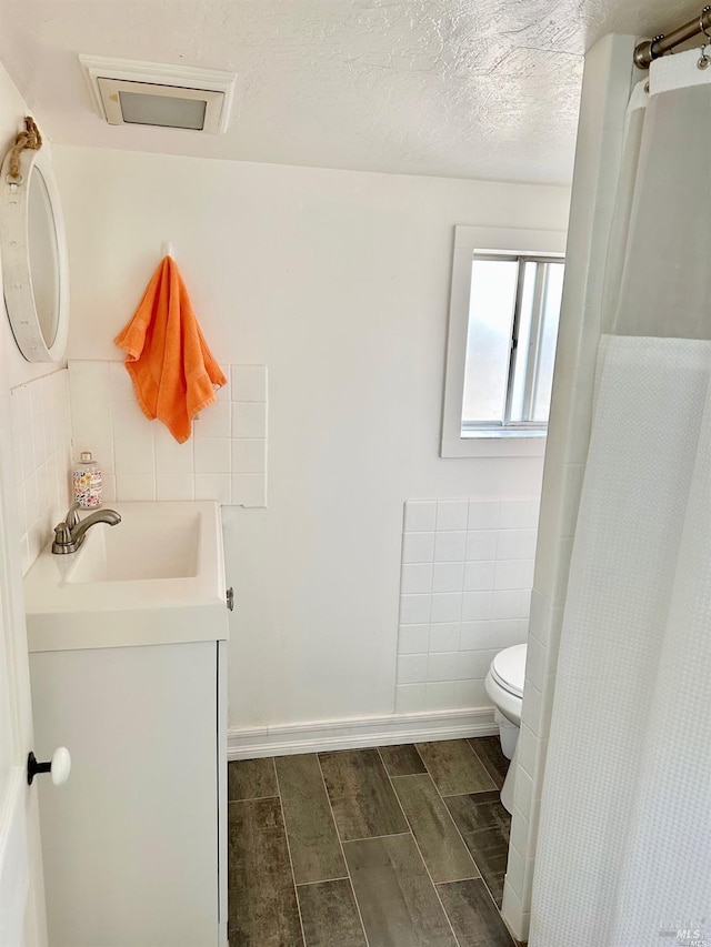 full bathroom with tile walls, visible vents, toilet, vanity, and a textured ceiling