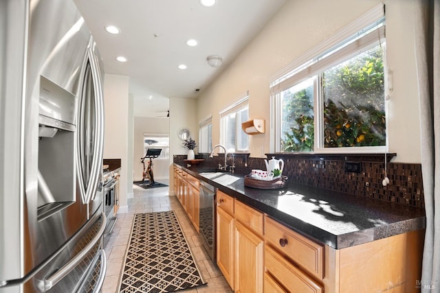 kitchen featuring dark countertops, backsplash, light brown cabinetry, appliances with stainless steel finishes, and a sink