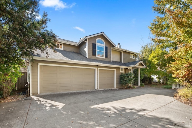 traditional-style house with a garage, concrete driveway, roof with shingles, and fence