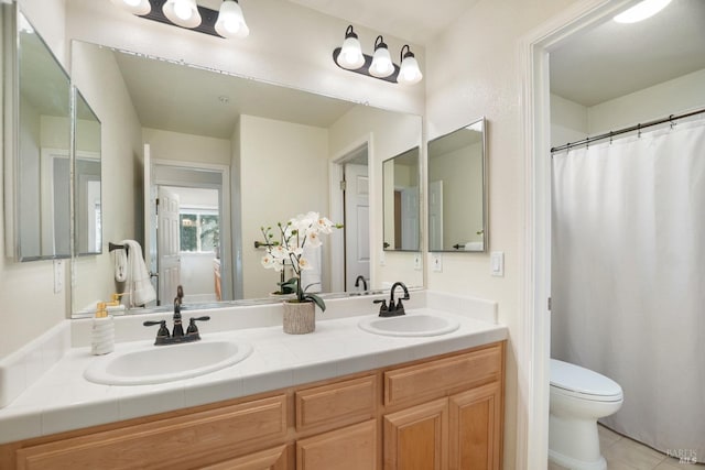 bathroom with double vanity, a sink, toilet, and tile patterned floors