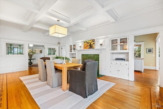 dining space featuring a fireplace, beamed ceiling, light wood-type flooring, and coffered ceiling