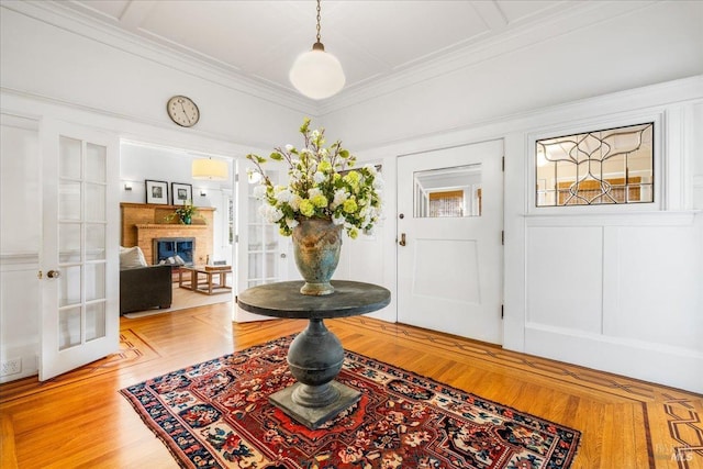 foyer entrance with french doors, light wood-type flooring, a glass covered fireplace, and crown molding