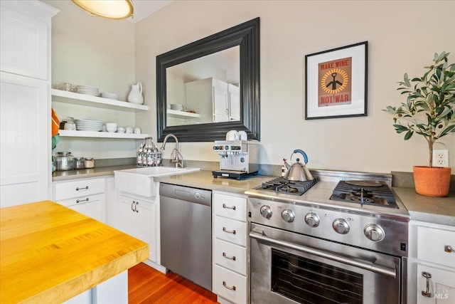 kitchen with appliances with stainless steel finishes, white cabinets, a sink, and wood finished floors