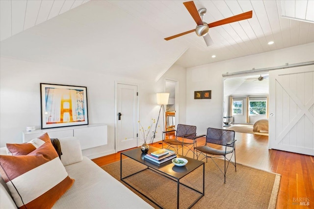 living area featuring lofted ceiling, ceiling fan, a barn door, and wood finished floors