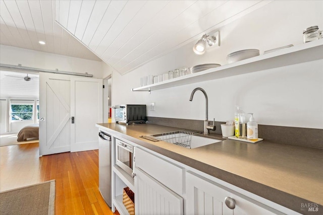 kitchen featuring a barn door, white cabinets, light wood-style floors, open shelves, and a sink