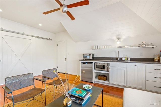 kitchen featuring a barn door, refrigerator, wood finished floors, stainless steel microwave, and dark countertops