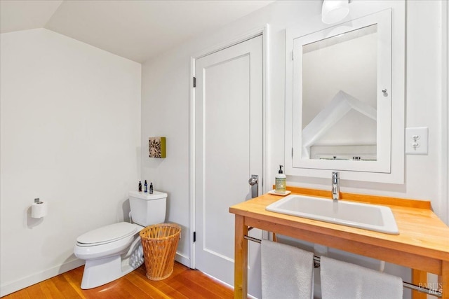 bathroom with toilet, vaulted ceiling, a sink, wood finished floors, and baseboards