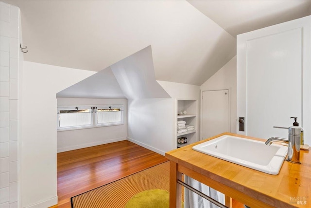 bathroom featuring baseboards, lofted ceiling, wood finished floors, built in shelves, and a sink