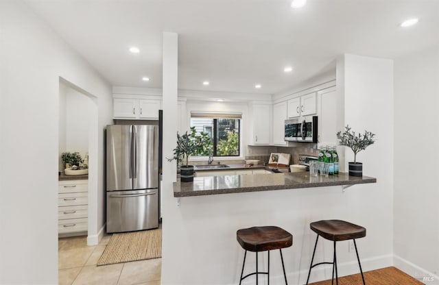 kitchen with a sink, white cabinetry, appliances with stainless steel finishes, dark stone counters, and a kitchen bar