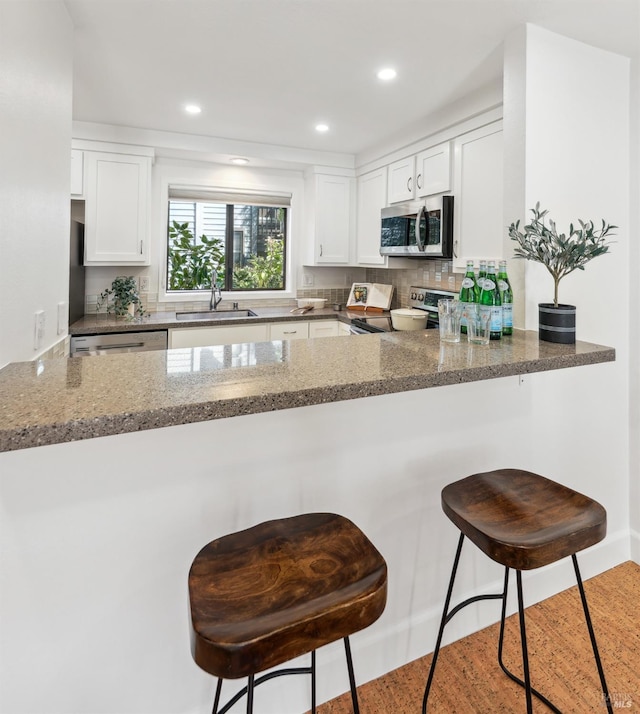 kitchen featuring dark stone counters, a peninsula, stainless steel appliances, white cabinetry, and a sink