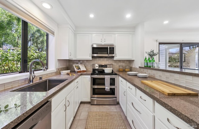 kitchen with tasteful backsplash, appliances with stainless steel finishes, white cabinets, a sink, and dark stone counters