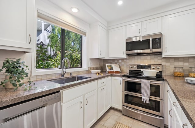 kitchen featuring light tile patterned floors, stainless steel appliances, backsplash, white cabinets, and a sink