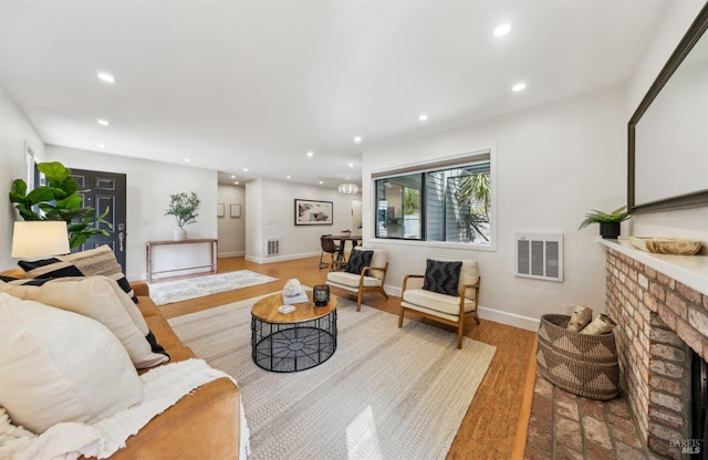 living area with recessed lighting, a brick fireplace, visible vents, and wood finished floors