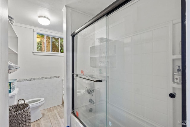 full bathroom with toilet, shower / bath combination with glass door, wood finished floors, tile walls, and wainscoting