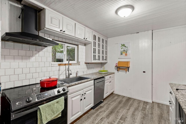 kitchen featuring tasteful backsplash, wall chimney exhaust hood, appliances with stainless steel finishes, light wood-type flooring, and white cabinetry