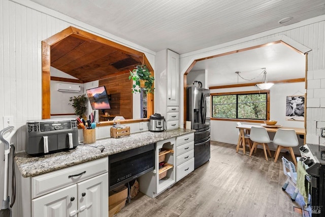 kitchen with a wall unit AC, light wood finished floors, white cabinetry, range with electric cooktop, and stainless steel fridge