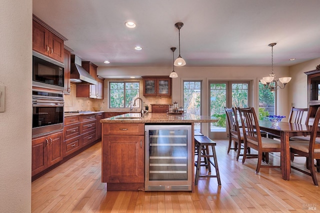 kitchen featuring wine cooler, appliances with stainless steel finishes, light wood-type flooring, wall chimney range hood, and a sink