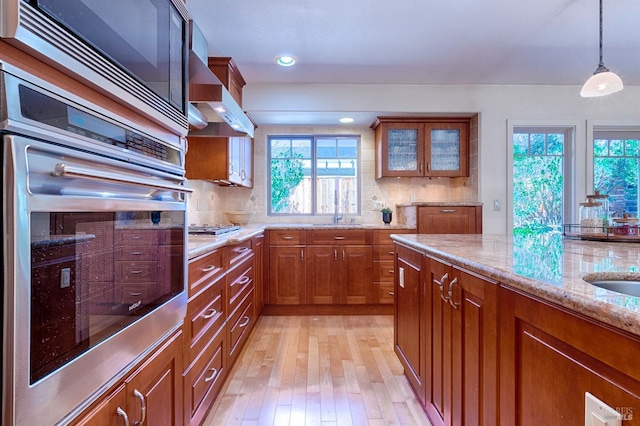 kitchen featuring stainless steel appliances, brown cabinetry, backsplash, and light stone counters