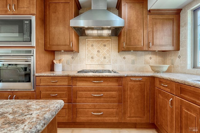 kitchen featuring appliances with stainless steel finishes, brown cabinetry, decorative backsplash, and island range hood