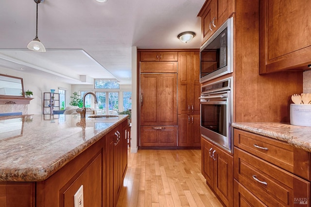 kitchen featuring light stone countertops, brown cabinets, a sink, and built in appliances