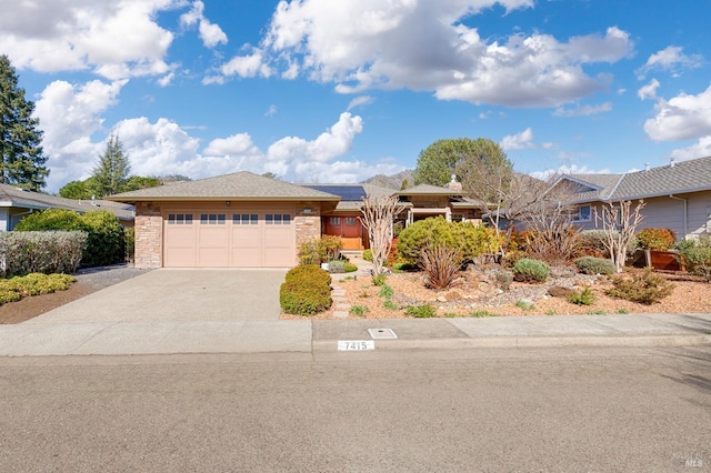 ranch-style home featuring a garage, stone siding, concrete driveway, and solar panels