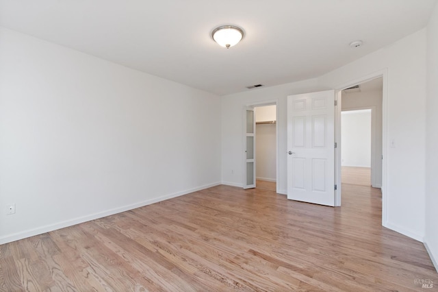 unfurnished bedroom featuring light wood finished floors, a walk in closet, visible vents, and baseboards