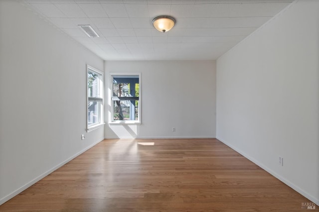 spare room featuring wood finished floors, visible vents, and baseboards