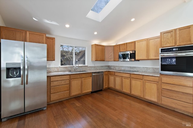 kitchen featuring vaulted ceiling with skylight, dark wood-style flooring, a sink, light countertops, and appliances with stainless steel finishes