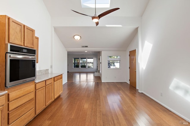 kitchen with baseboards, lofted ceiling with skylight, light wood-style flooring, open floor plan, and stainless steel oven