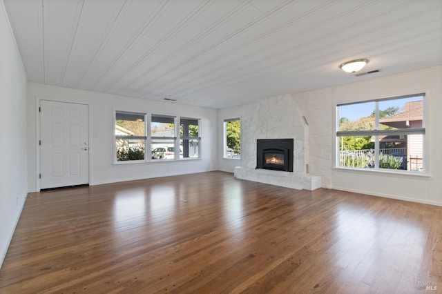 unfurnished living room featuring a healthy amount of sunlight, visible vents, wood finished floors, and a stone fireplace