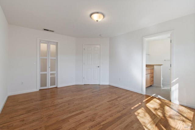 unfurnished bedroom with light wood-type flooring, baseboards, visible vents, and ensuite bathroom