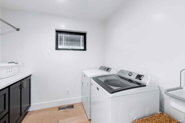 laundry room featuring light wood finished floors, cabinet space, visible vents, washing machine and dryer, and a sink