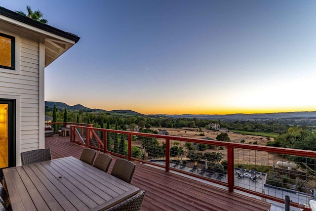 deck at dusk featuring a mountain view and outdoor dining space