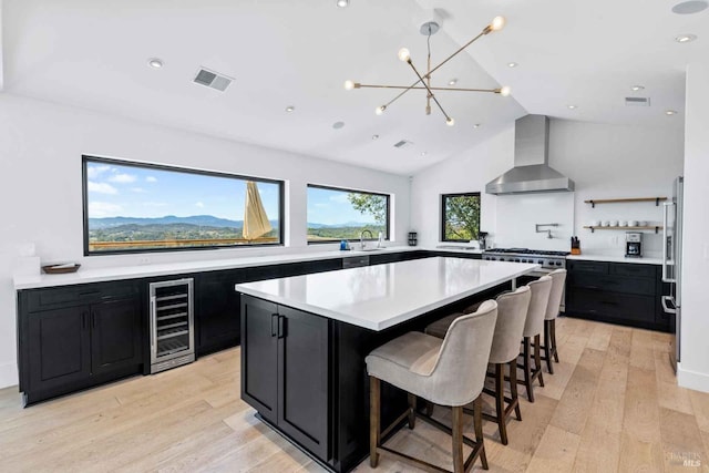 kitchen featuring dark cabinets, beverage cooler, a kitchen island, visible vents, and wall chimney range hood