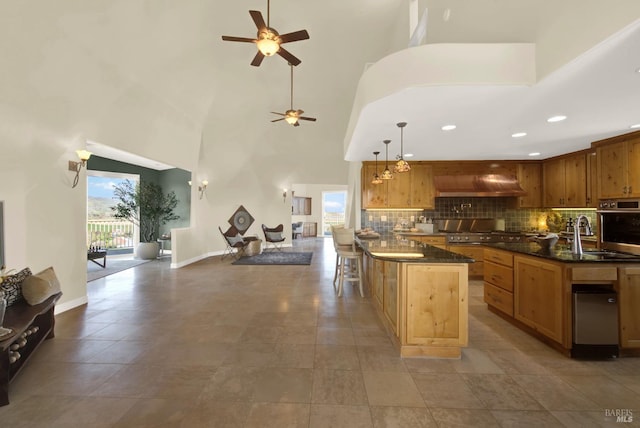 kitchen featuring tasteful backsplash, wall chimney exhaust hood, open floor plan, stainless steel oven, and a sink