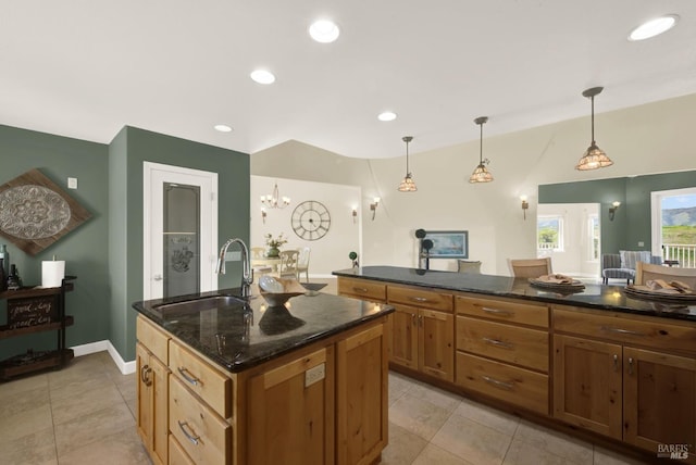 kitchen with recessed lighting, decorative light fixtures, a sink, dark stone countertops, and a center island with sink