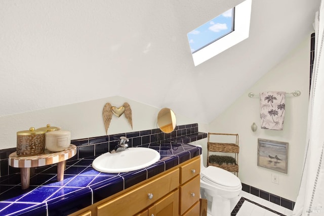 bathroom with vaulted ceiling with skylight, tile patterned flooring, vanity, and toilet