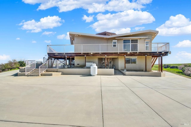 view of front of house with stucco siding, a wooden deck, stairway, and a patio