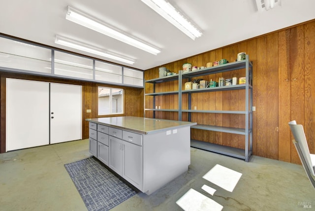 interior space featuring concrete flooring, a center island, wooden walls, and open shelves