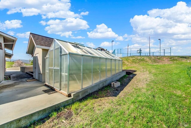 exterior space featuring a shingled roof, a greenhouse, a yard, and an outbuilding