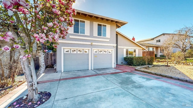 traditional-style home featuring an attached garage, fence, concrete driveway, and stucco siding